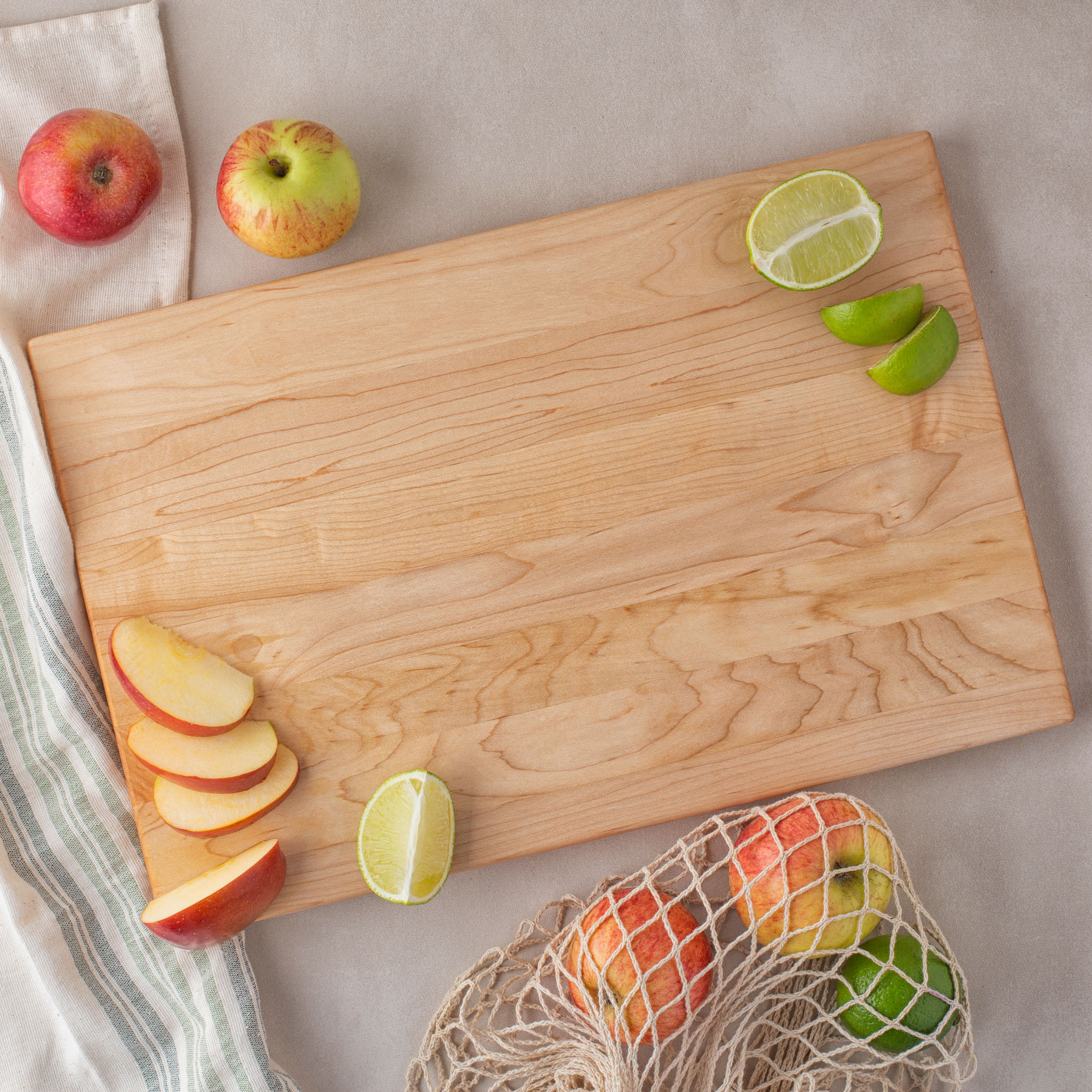 A wooden cutting board with apples and limes on it.