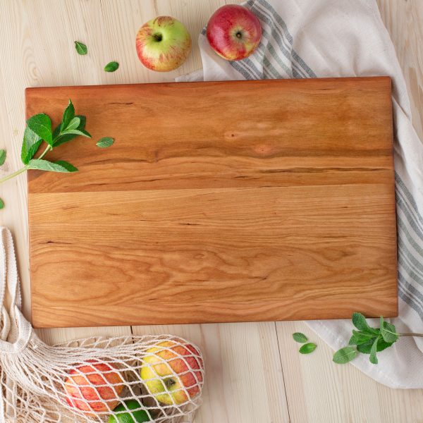 A wooden cutting board with apples and a bag of apples.