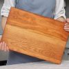 A woman is holding a wooden cutting board.