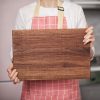 A woman is holding a wooden cutting board.
