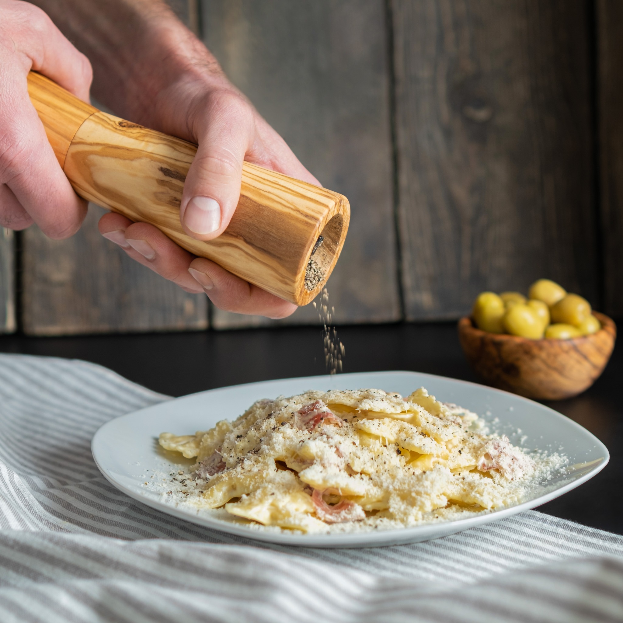 A person grinding a pepper mill on a plate of pasta.