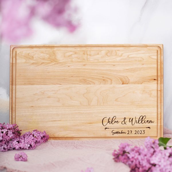 A wooden cutting board with the name of the bride and groom on it.