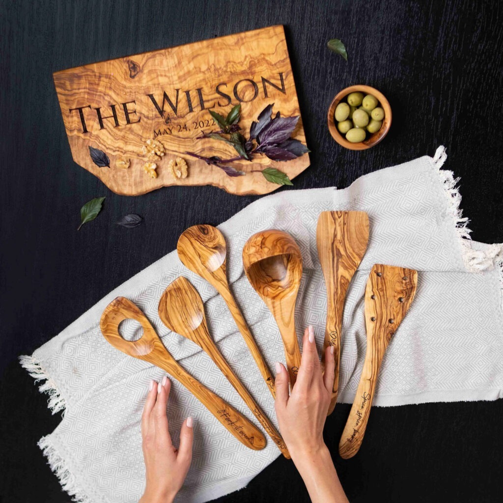 Set of 6 personalized olive wood utensils with a personalized live edge charcuterie board next to them.