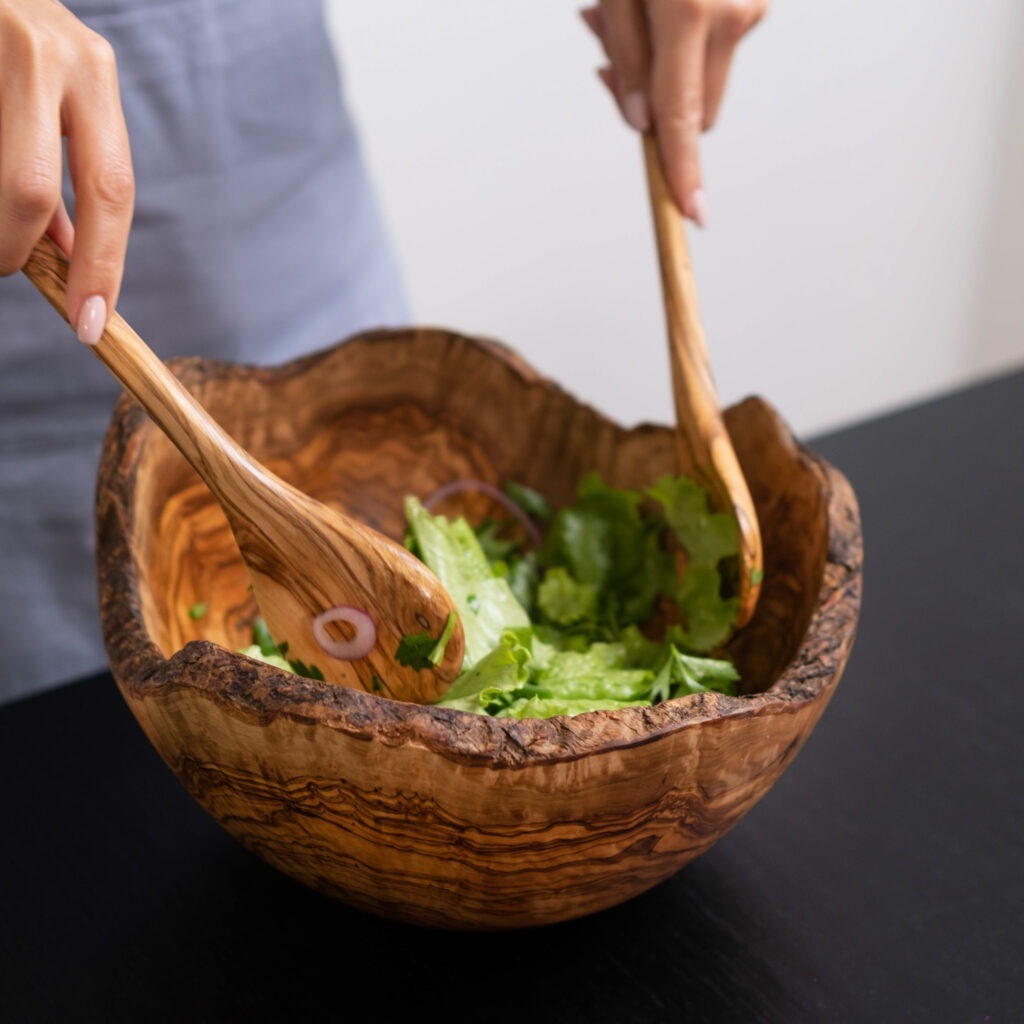 A woman is holding wooden spoons in a wooden bowl.