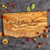 Personalized olive wood live edge cheese board laying on top of a kitchen counter surrounded by pieces of fruit.
