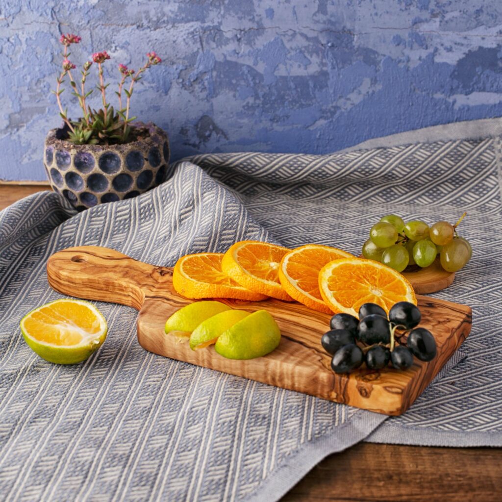 An Olive Wood Paddle Board with oranges and grapes on it.