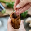 A person's hands grinding salt into a wooden pepper mill.