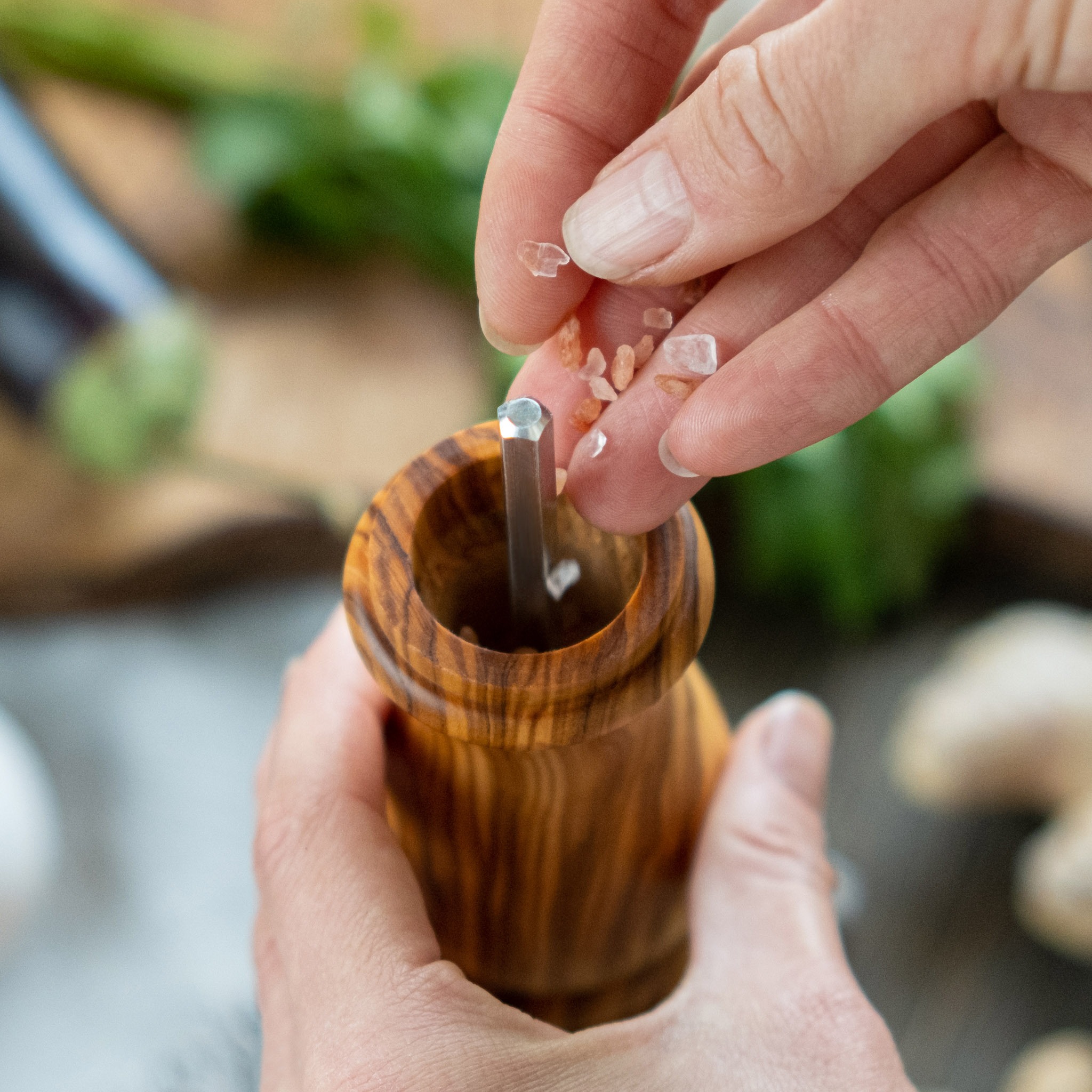 A person's hands grinding salt into a wooden pepper mill.