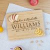 Personalized cutting board with the names "stephen & michelle williams" and the date "10.15.2013," surrounded by sliced fruit and nuts on a kitchen countertop.