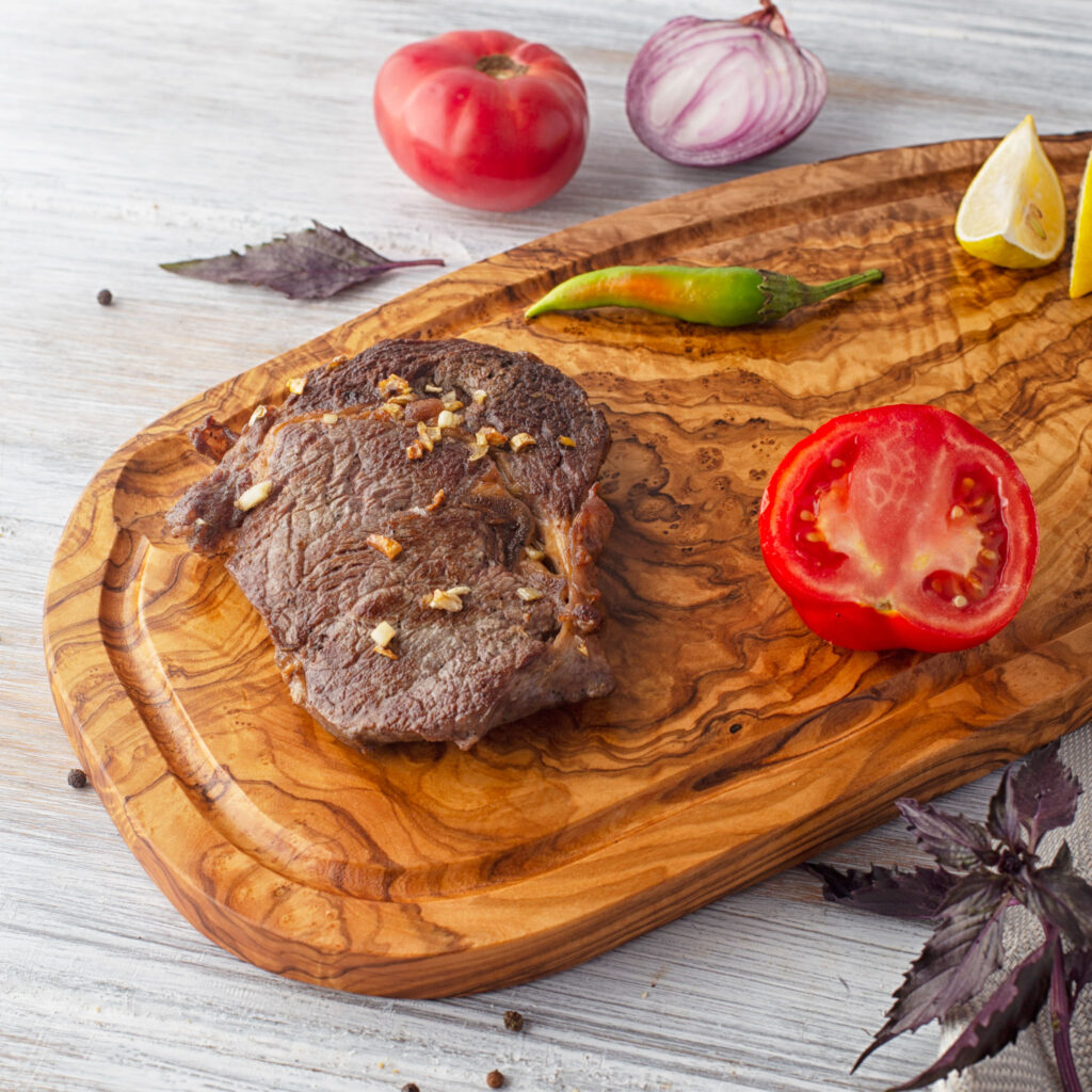 An Olive Wood Board with Juice Groove with a steak on it.