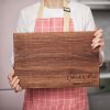 A woman is holding a wooden cutting board.