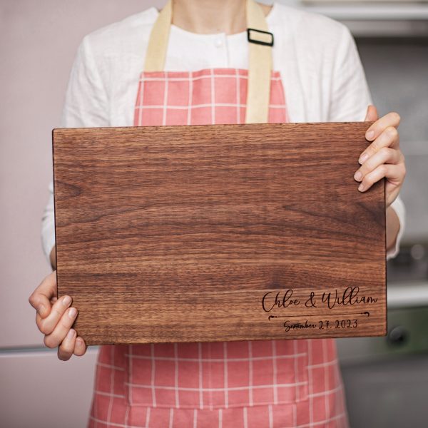 A woman is holding a wooden cutting board.